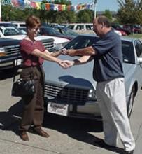 Seller and car dealer shaking hands and handing over keys.
