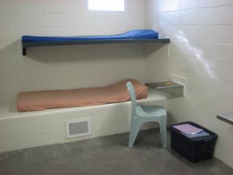 A typical jail cell with bunk beds, a chair and storage tote.