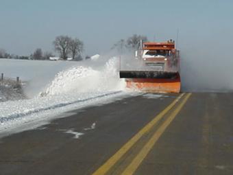 County truck plowing snow off the road into the ditch.