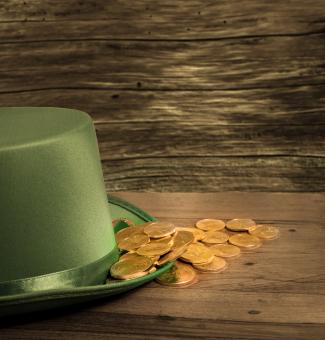 Treasure of pure gold coins inside the rim of a green velvet hat. Placed on wooden table to celebrate luck on St Patrick's Day o