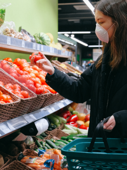 This is an image of a woman shopping for vegetables wearing a medical face mask. 