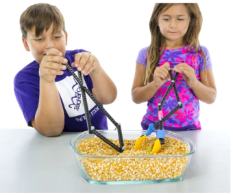 two kids using grabbers to pick up dried corn