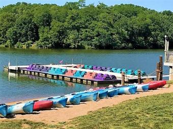 Multiple kayaks accress the sand portage with paddleboats parked at the dock on the lake.