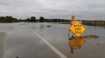 "Water Over Road" sign on roadway submerged in water.